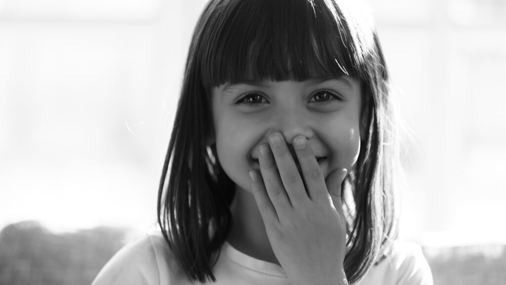 Funny,Shy,Little,Girl,Laughing,Covering,Mouth,With,Hand,Looking